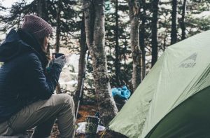 A woman holding a mug sitting outside of a tent in the woods. | Camping near Sherwood, AR.