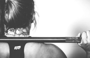 The back of the head and shoulders of a woman holding a barbell wearing a sports bra. | Fitness around Sherwood, AR.