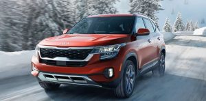 A red 2022 Kia Seltos being driven on the road with snow-laden trees in the background. | Kia dealer in Sherwood, AR.